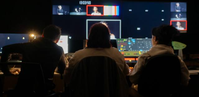 crew at a live-broadcast control desk, wall of monitors